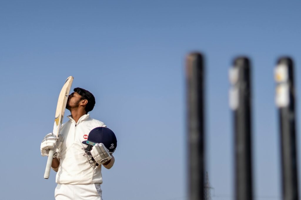 Cricket player in uniform celebrating a game-winning shot by kissing his bat on a sunny day.