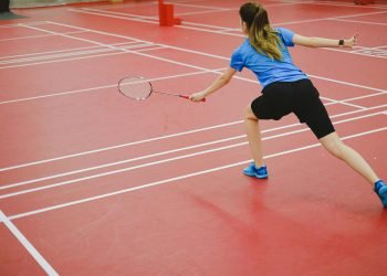 Back view of a woman playing badminton on an indoor court. Action shot capturing skill and movement.